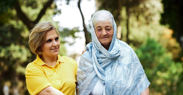 A woman in a yellow tshirt walking with an older woman wearing a shawl over her head and shoulders.