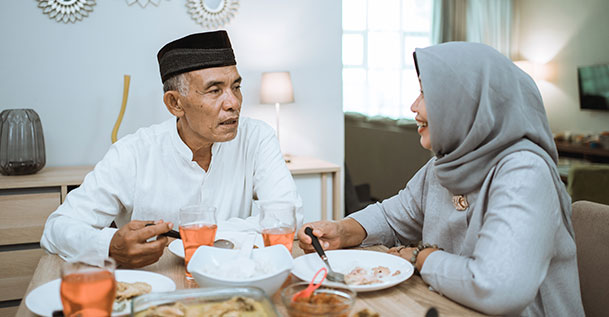 An elderly Arabic couple sitting at a table eating a meal.