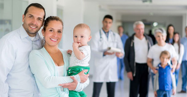 A couple holding a baby in a hospital corridor with hospital staff standing behind them.