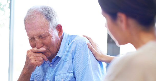 A woman consoling an elderly man in a blue shirt.
