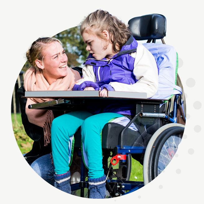 A woman kneeling beside a young girl in a wheel chair.