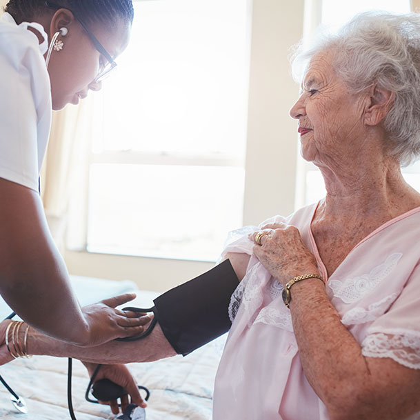 An elderly woman in a nightgown having her blood pressure taken by an African American nurse.