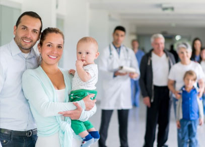 A young couple holding a baby in a hospital corridor with hospital staff standing behind them.