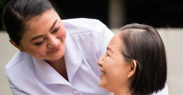 A female nurse in a white uniform smiling at a middle-aged woman.
