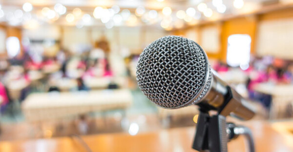 A close up of a microphone with a blurred conference in the background.